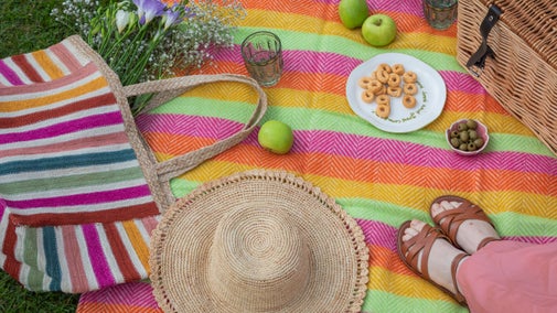 A picnic scene with a blanket, a basket filled with food, and a pair of shoes resting beside it.